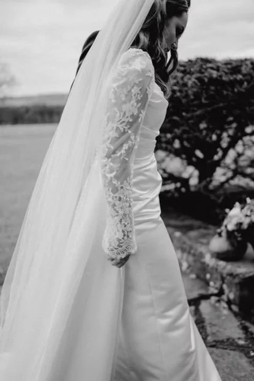 Detail of a lace sleeve and cathedral-length veil on a satin wedding dress, in black and white