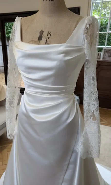 Draped satin wedding gown with lace sleeves on a dress stand in the studio