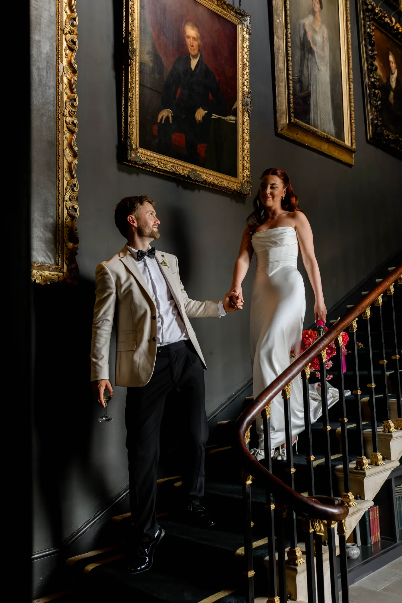 Georgie walking down a grand staircase with her groom, the lace top removed to show her strapless draped satin gown