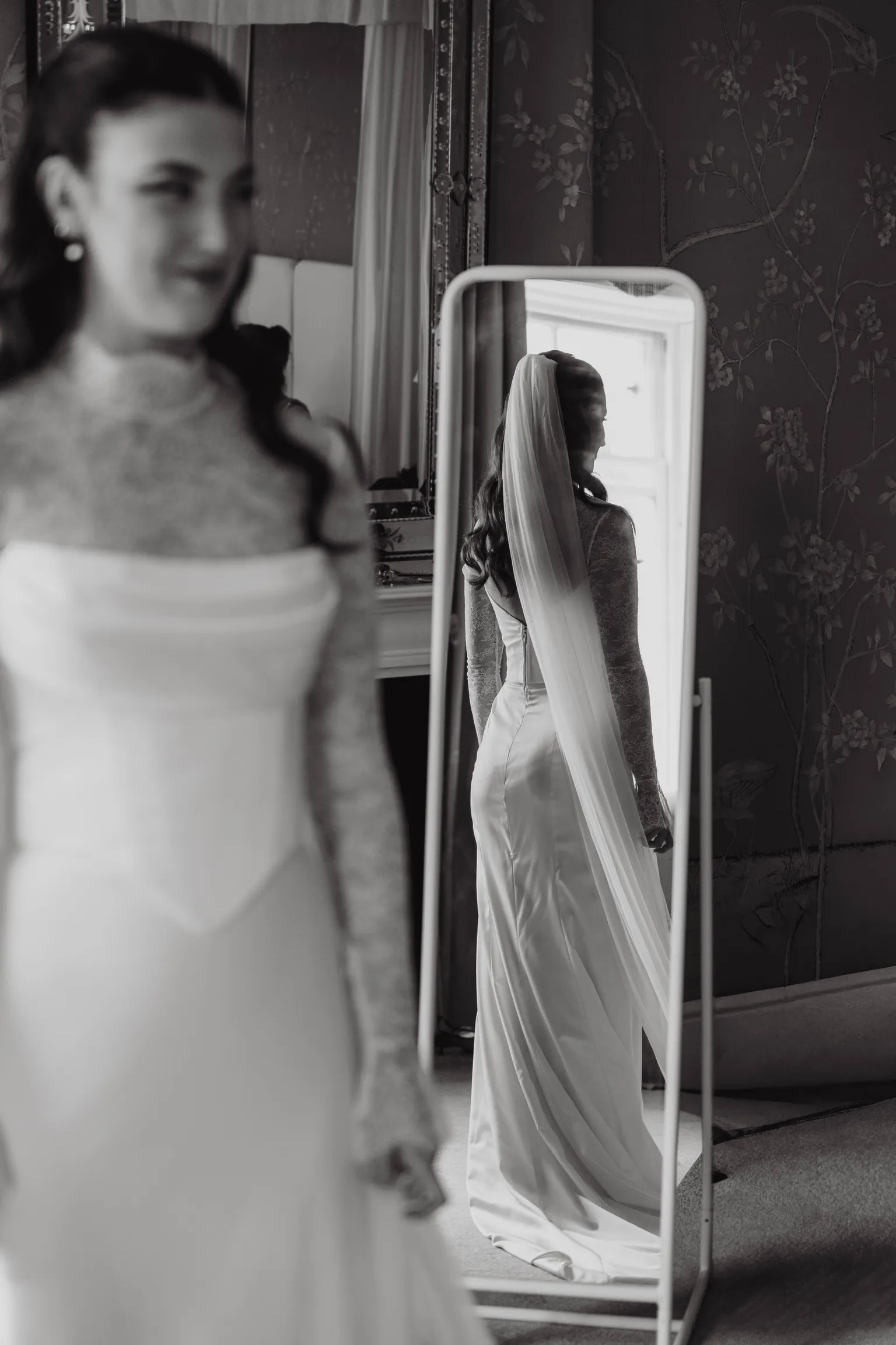 Georgie reflected in a mirror from behind, her cathedral veil falling over the Chantilly lace top and fitted satin skirt