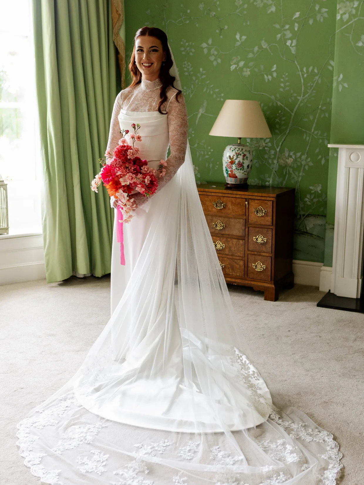 Custom ivory satin wedding dress with a high-neck Chantilly lace top, full-length view with her lace-edged cathedral veil spread across the floor