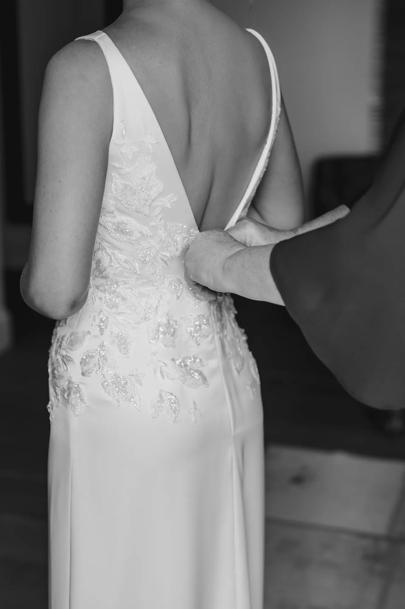 Back view of Tasha’s beaded satin gown being fastened, showing the low V back and sequinned floral appliqué