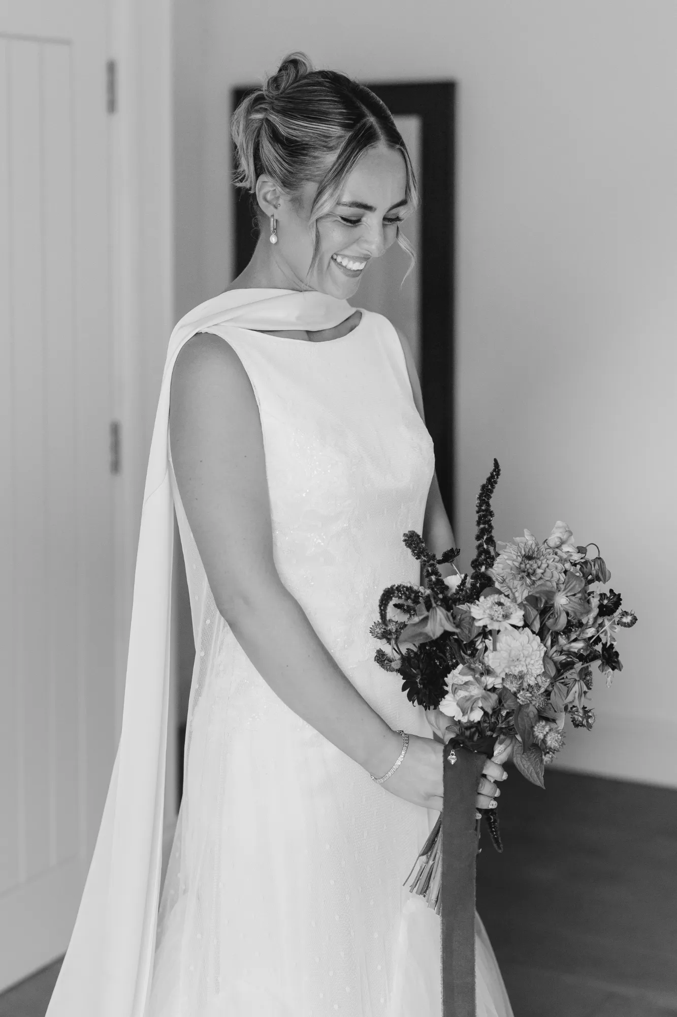 Custom spot tulle wedding overdress with a draped neck sash, Tasha smiling down at her bouquet