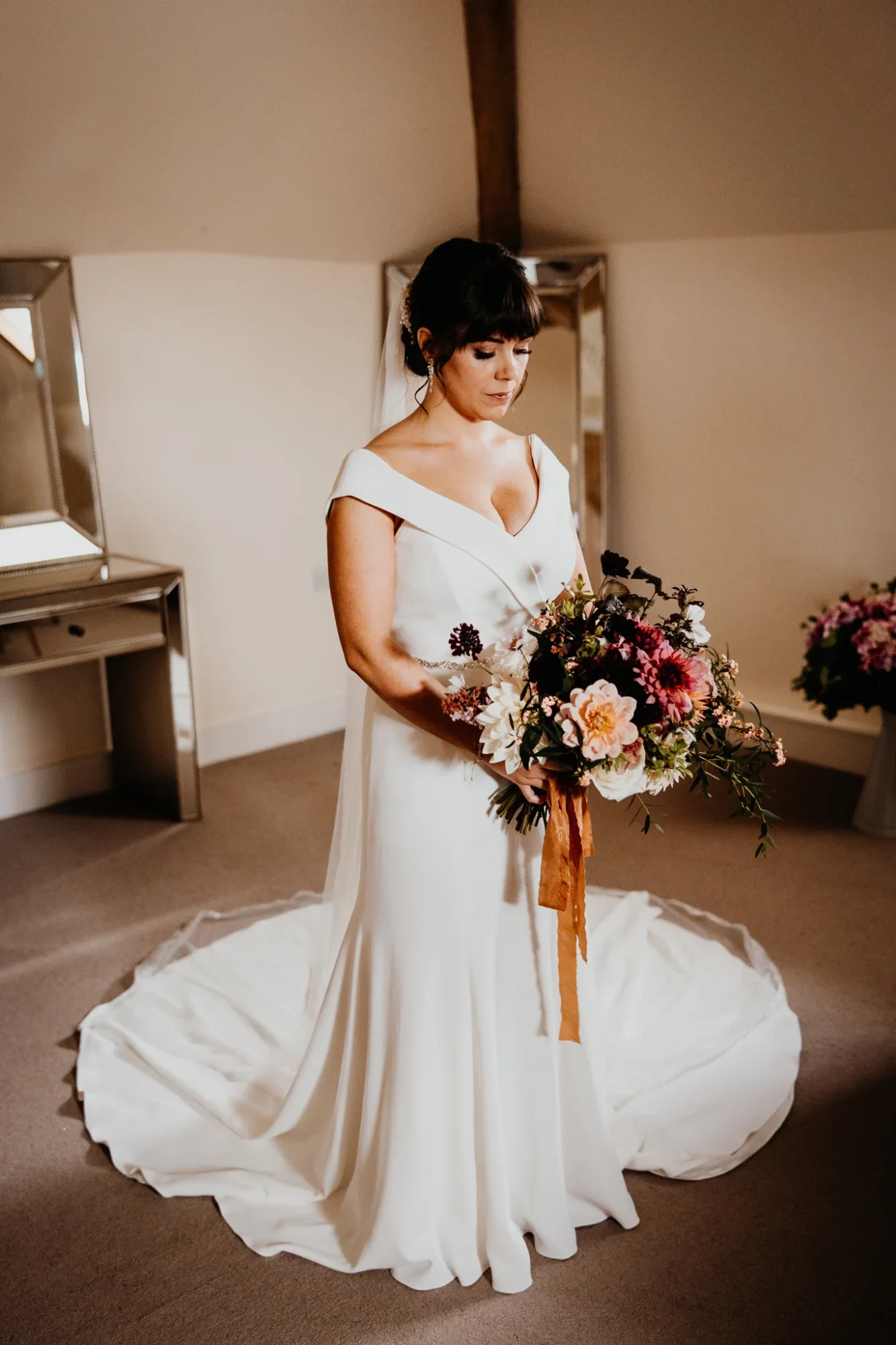 Kate in her ivory crepe fit-and-flare wedding dress with an off-shoulder neckline and cathedral veil, holding an autumnal bouquet
