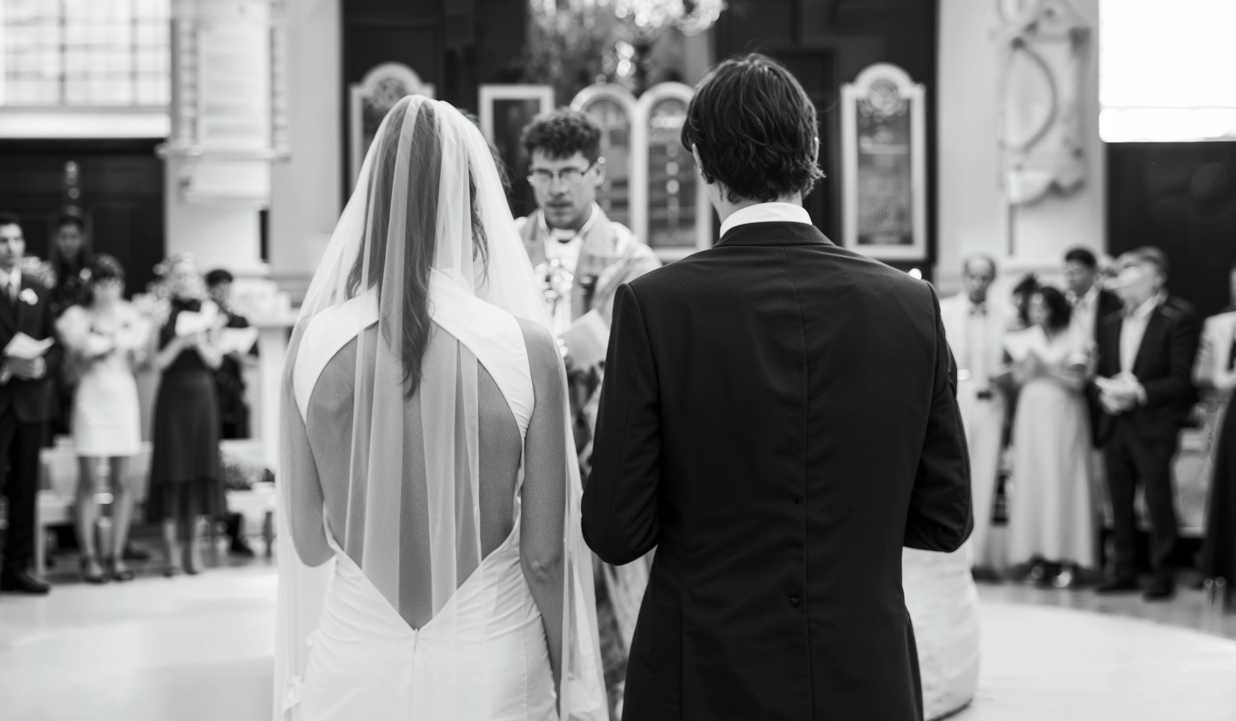 Bride and groom at the altar of their church ceremony, the bride in a keyhole-back satin wedding dress beneath a full-length veil