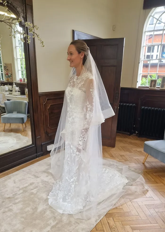 Bride at her final fitting in an all-over lace wedding dress with sheer sleeves and a full-length veil