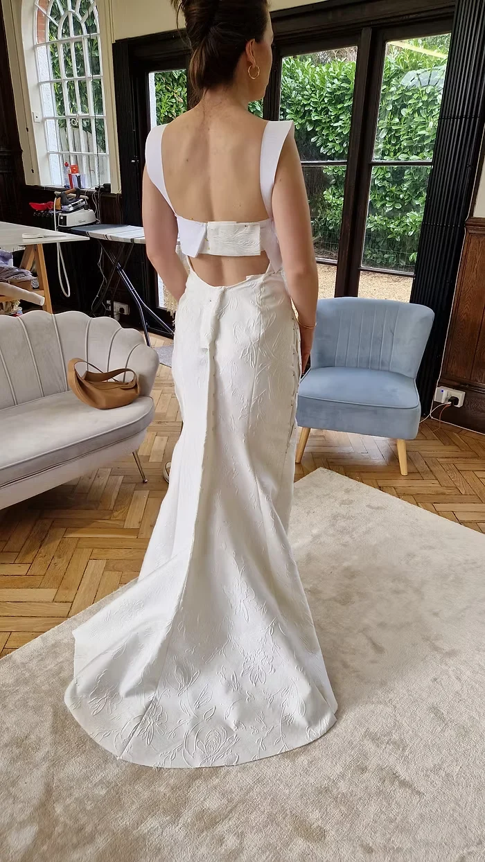 Back view of a wedding dress toile on a bride, the open back and fitted train pinned before the final fabric is cut